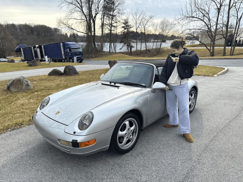 A happy customer with her late 90s Porsche Convertible delivered by an enclosed door-to-door transport trailer in the background to her door.